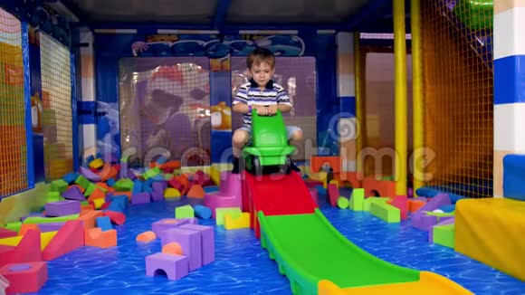 乐笑小男孩骑在玩具塑料车上的视频来自游乐园的彩色滑梯视频的预览图