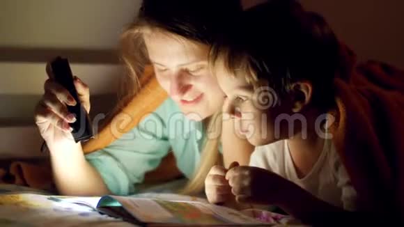 小母亲在睡觉前给小儿子读故事书时手持火炬的特写视频视频的预览图