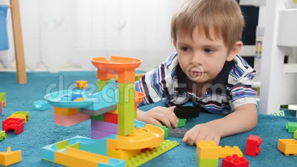 特写4k视频快乐的微笑男孩一边玩一边看由五颜六色的积木和砖块制成的大理石跑视频的预览图
