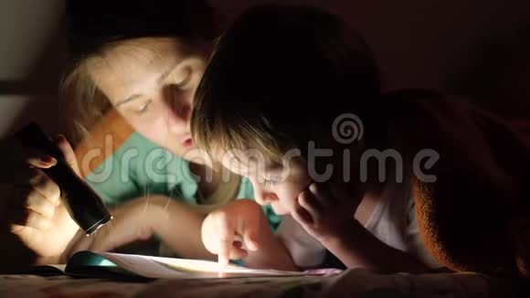 特写4k小男孩晚上和妈妈躺在床上用火把看书的视频视频的预览图