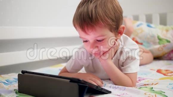 4k小男孩躺在床上用数码平板电脑浏览互联网的视频视频的预览图