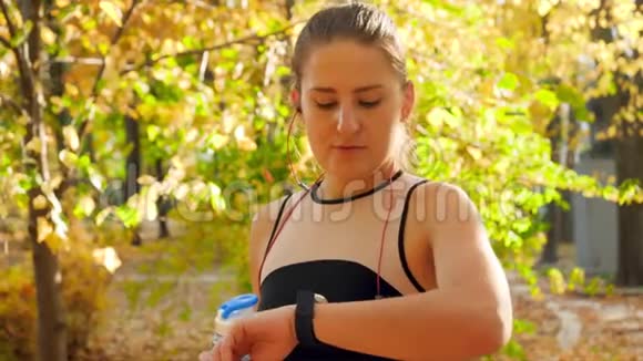 4k视频美丽微笑的年轻女子在公园里做运动看完她的智能健身后喝水视频的预览图