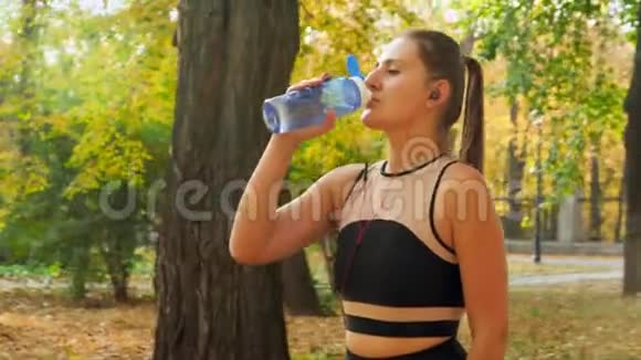 4k镜头在秋日健身运动结束后穿着运动服喝酒的美女周围飞舞视频的预览图