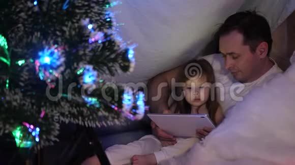 父亲和女儿在圣诞节晚上在平板电脑上玩和看动画片在孩子们的房间里有一个帐篷里面有一个帐篷视频的预览图