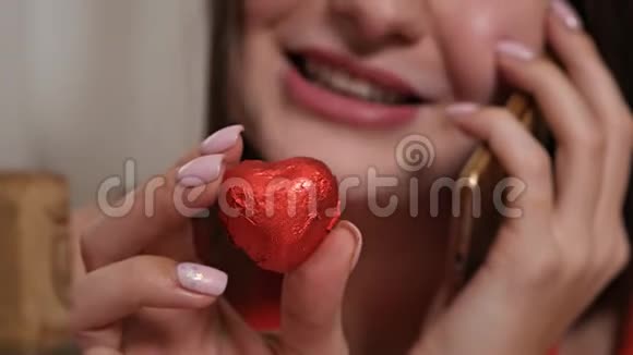 一个女孩的特写脸一个女孩在电话里说话手里拿着一颗红色心形巧克力糖果视频的预览图