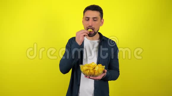 一个穿着蓝色衬衫和白色T恤的年轻人吃辛辣的薯片用一杯水把它们熄灭视频的预览图