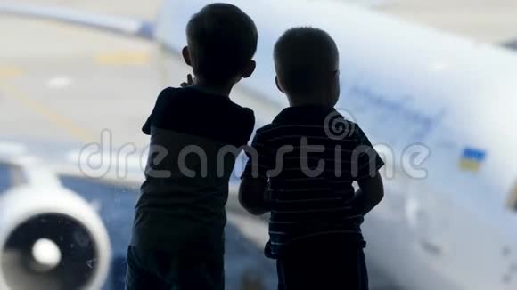 两个小男孩在机场候机楼的大窗户外等待登机的剪影片段视频的预览图