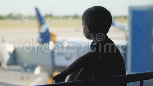 小男孩坐在机场候机楼的大窗户旁边看喷气式飞机的剪影视频视频的预览图