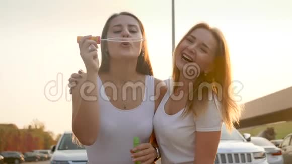 4K慢动作视频两个女孩在日落时一起玩在街上吹肥皂泡视频的预览图