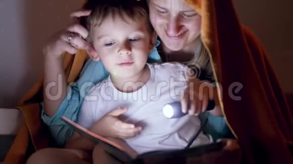 4k视频快乐微笑的母亲和小儿子晚上坐在毯子下用手电筒看书视频的预览图