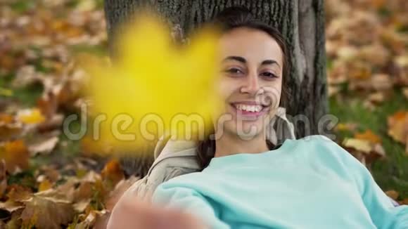 在秋天公园里美丽的年轻兴高采烈地微笑着的女人与明亮的橙色叶子玩耍视频的预览图