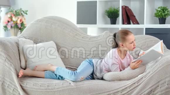 忙碌的体贴的年轻的女孩子在舒适的客厅里躺在沙发上看书视频的预览图