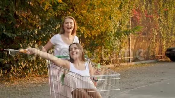 4K慢动作视频两个笑着的女孩坐在购物车里在大商场的停车场吹肥皂泡视频的预览图