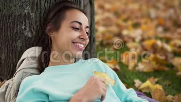 在秋天公园里美丽的年轻兴高采烈地微笑着的女人与明亮的橙色叶子玩耍视频的预览图