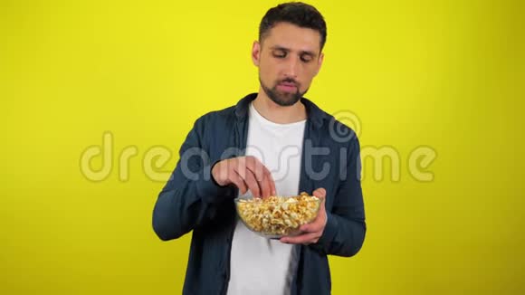穿着蓝色衬衫和白色T恤的年轻人吃透明玻璃盘子里的爆米花不好吃不喜欢视频的预览图