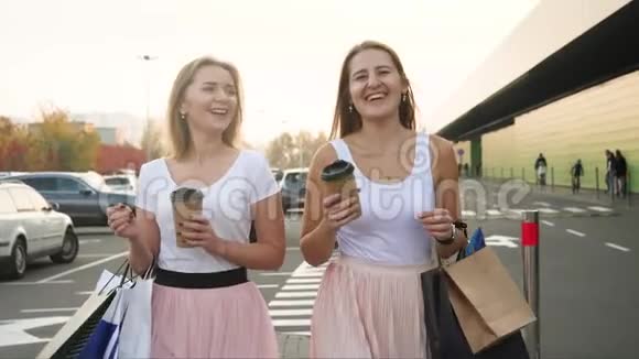 两个笑的女朋友拿着很多纸袋走出购物中心喝咖啡的视频视频的预览图
