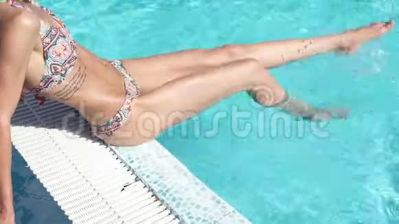 美丽的年轻女子泼水双腿坐在池边视频的预览图