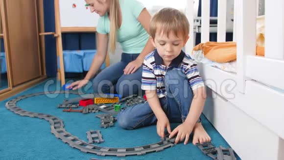 4k视频年轻母亲和她的小儿子在卧室的地板上玩玩具铁路视频的预览图