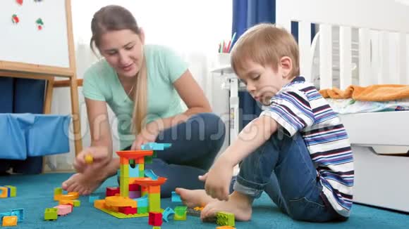 快乐妈妈和微笑的小男孩在卧室的地毯上玩的4k视频一家人在家玩大理石视频的预览图