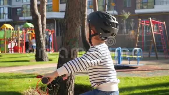 在大型儿童游乐场旁边的公园里小男孩骑着自行车戴着防护头盔的特写4k视频视频的预览图