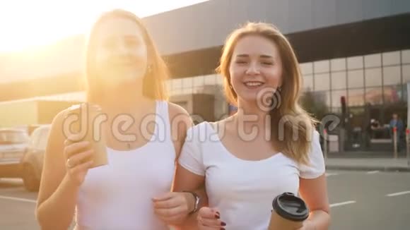 特写4k视频两个快乐的女孩在购物中心的停车场散步时微笑交谈和喝咖啡视频的预览图