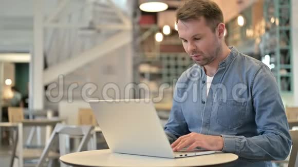 在咖啡馆使用笔记本电脑头痛的休闲男士视频的预览图