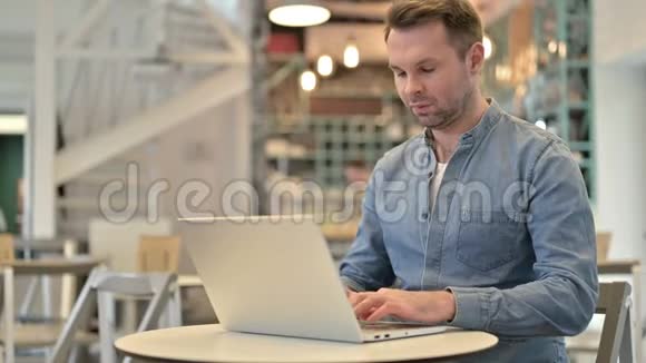 在咖啡馆使用笔记本电脑时腰痛的休闲男士视频的预览图