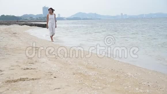 开朗的亚洲女人光着脚在热带夏季海滩散步女人在海滩上沿着海水和沙子的波浪行走享受享受乐趣视频的预览图