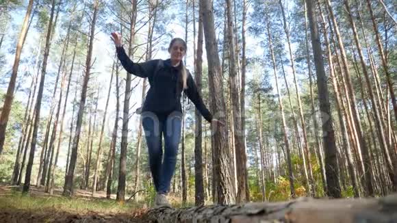 4k视频美丽的年轻女徒步旅行者背包行走在倒下的树上平衡在森林的大原木上视频的预览图