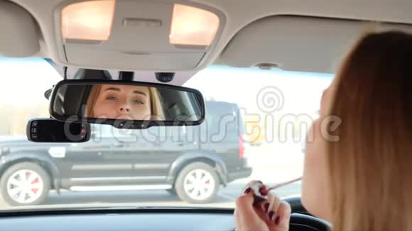 年轻女性坐在车里用后视镜涂唇膏和化妆视频的预览图