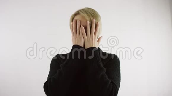 成年白种人白种人金发女人在明亮的白色背景下站着用手掌闭上脸视频的预览图