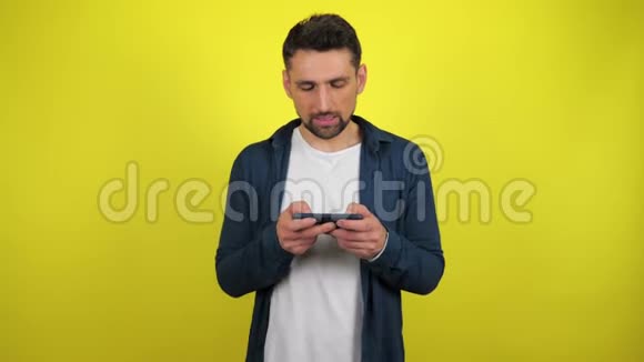 一个穿着蓝色衬衫和白色T恤的年轻人在智能手机上玩游戏输了心烦意乱视频的预览图