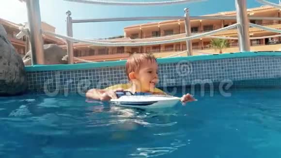 4k快乐微笑小男孩带着充气圈在酒店游泳池里玩玩具船的视频视频的预览图