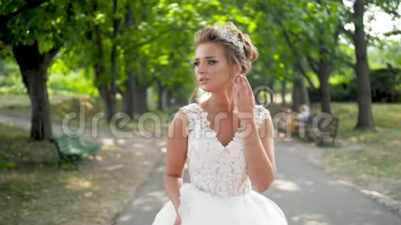 年轻的微笑新娘穿着漂亮的婚纱在大树下的公园里散步视频的预览图