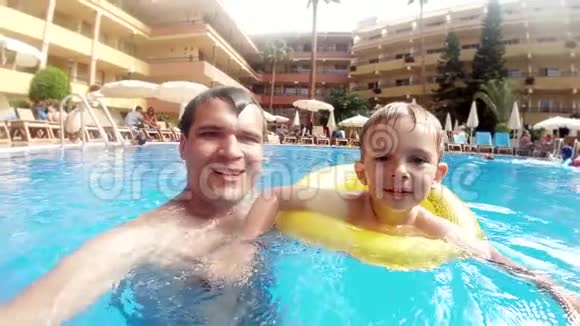 在酒店度假胜地的室外游泳池里爸爸和小儿子一起快乐地微笑和大笑的慢动作视频视频的预览图