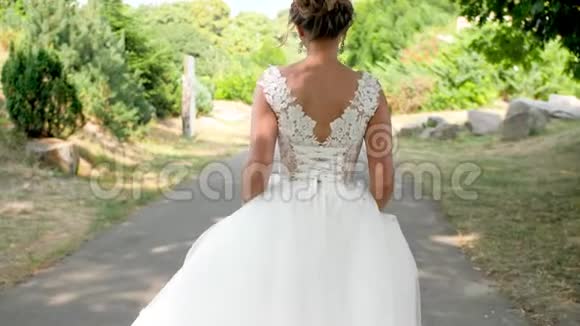 4K慢镜头视频年轻美丽的新娘穿着白色长裙在公园的小路上走视频的预览图
