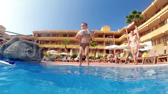 酒店度假村游泳池里带充气环跳泳的小男孩慢动作视频视频的预览图