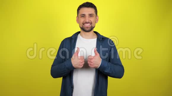 一个穿着蓝色衬衫和白色T恤的年轻人看着相机微笑着用双手表现出来视频的预览图