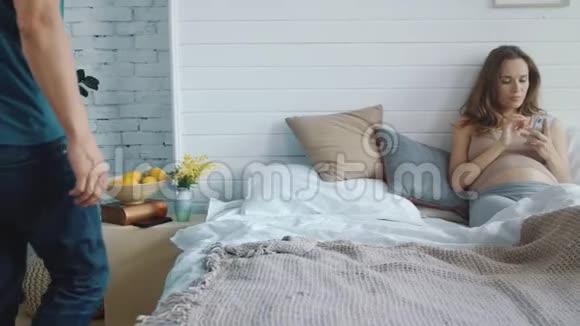 漂亮的孕妇在发智能手机短信快乐的孕妇躺在床上视频的预览图