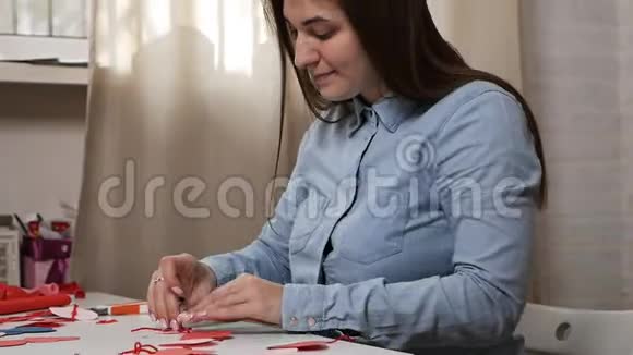 创意女孩用剪刀剪出红纸心花为情人制作明信片视频的预览图