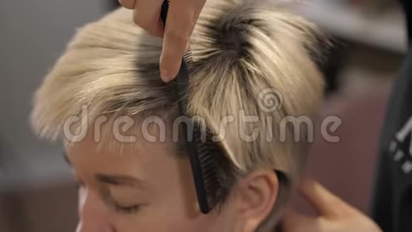 一位美发店的发型师检查一位金发女郎的头发根视频的预览图