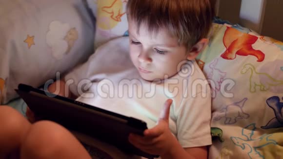 特写4k小男孩晚上躺在床上在平板电脑上玩电子游戏的镜头视频的预览图