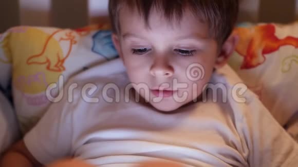 特写4k视频4岁小男孩晚上躺在床上看平板电脑视频的预览图