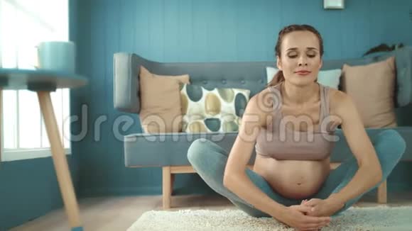 特写微笑孕妇在家练习产前瑜伽视频的预览图
