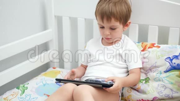 4K小男孩早上坐在床上使用数码平板电脑视频的预览图