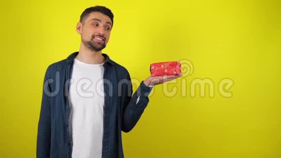一个穿着白色T恤的年轻人看着手里的礼物微笑着黄色的背景视频的预览图