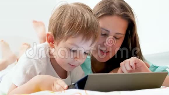 4k特写视频年轻母亲和蹒跚学步的儿子躺在一起用平板电脑教他玩视频的预览图