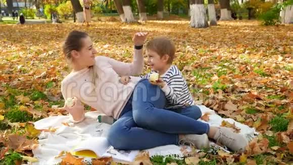带着年轻妈妈躺在秋天公园的毯子上吃苹果的笑笑小男孩4k视频视频的预览图