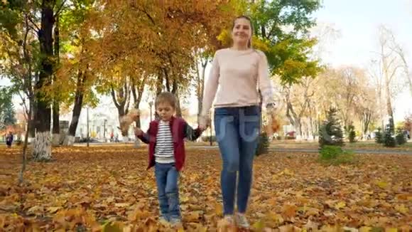 4k视频快乐微笑的妈妈和小儿子在秋天公园的草地上走着上面覆盖着黄叶视频的预览图