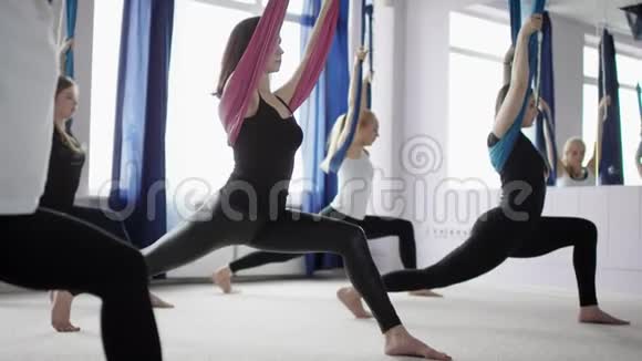 在反重力瑜伽工作室中中等水平的年轻女性在吊床上练习空中瑜伽视频的预览图